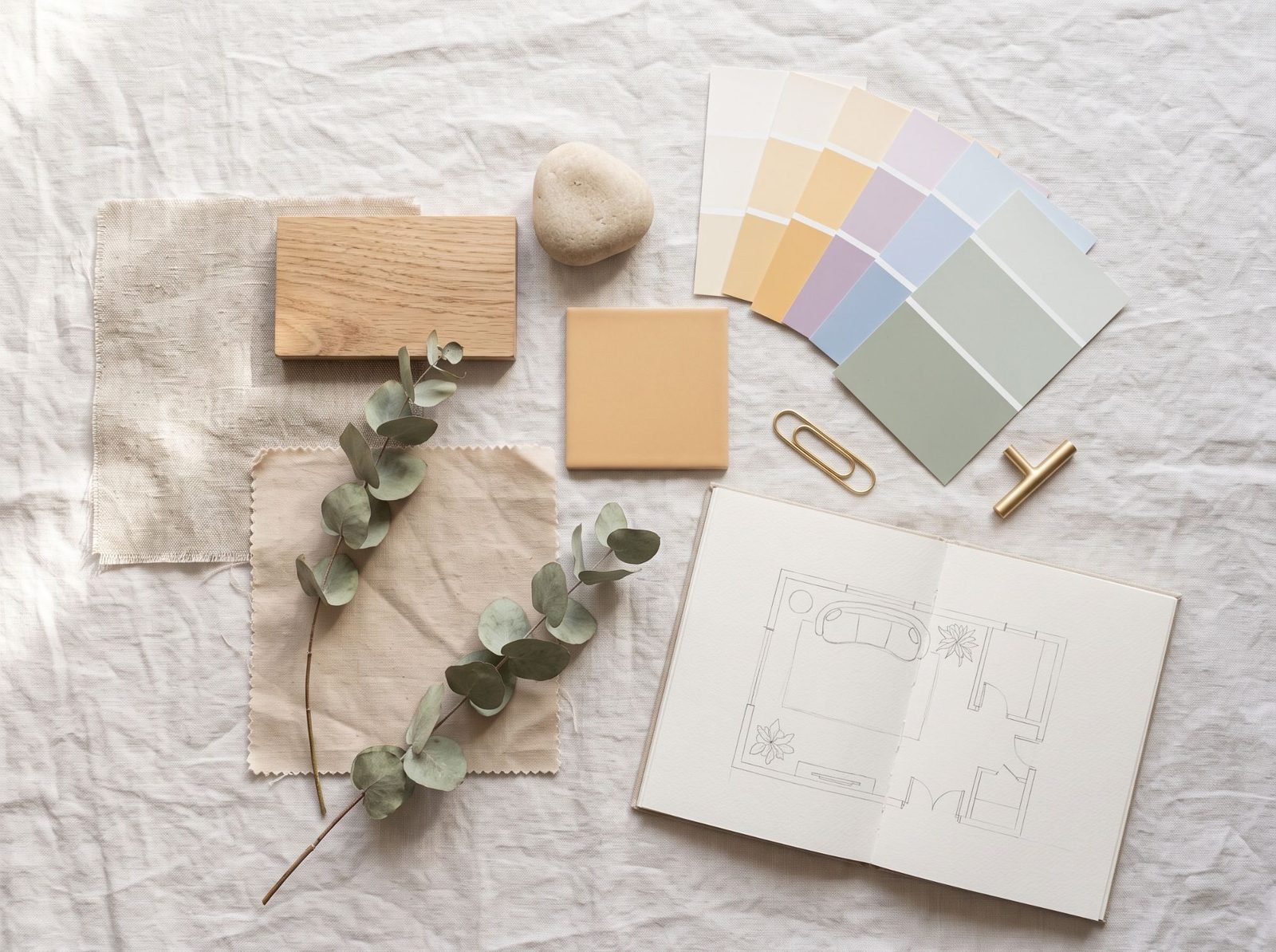 Une planche d’ambiance : échantillons de lin, de bois clair et de pierre, carreau ocre, nuancier de couleurs douces, eucalyptus et croquis de plan
